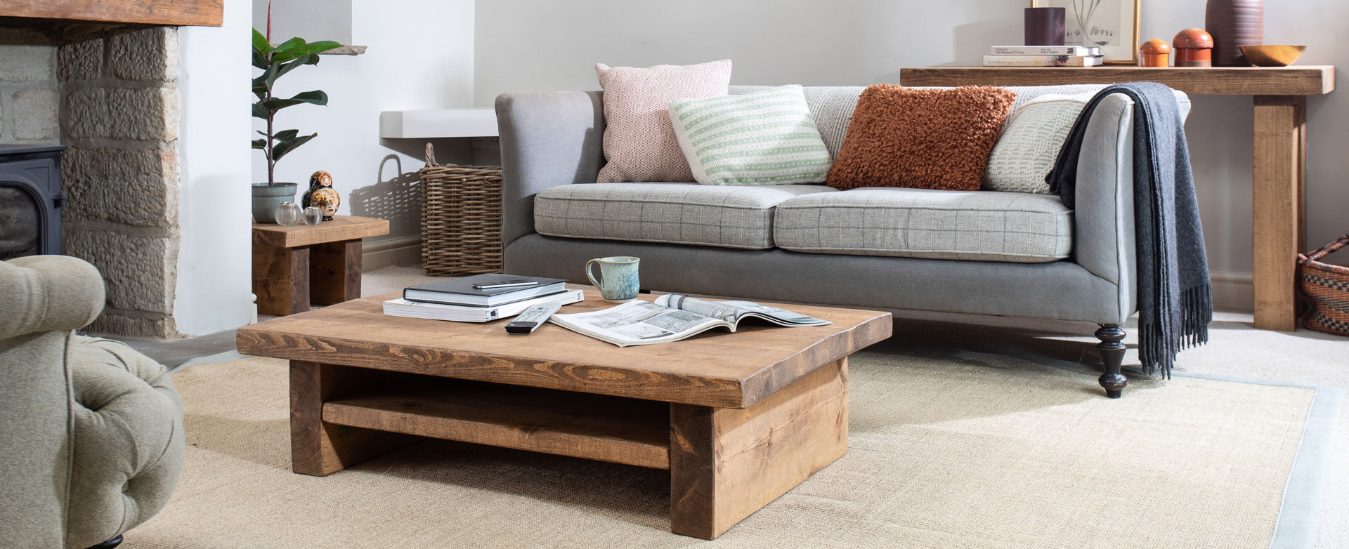 rustic sandstone wall in a hallway, at dusk, with a wooden console table, dressed with a circular mirror, and surrounded by wellies, blankets in wire baskets and a table lamp giving off a warm glow