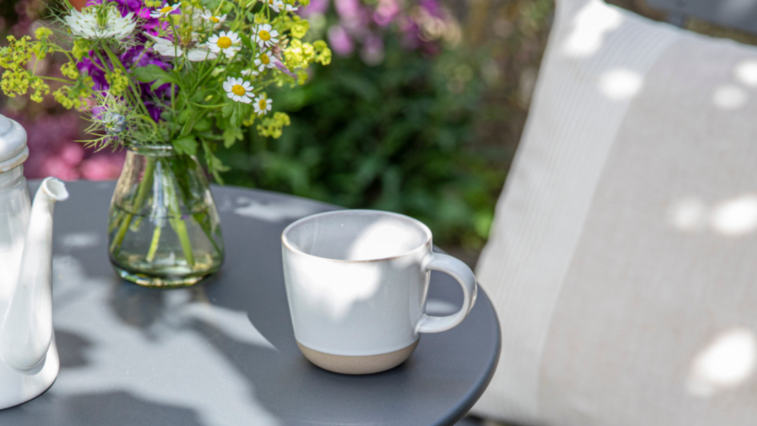 Teacup and vase of flowers on a grey metal tabletop outdoors.