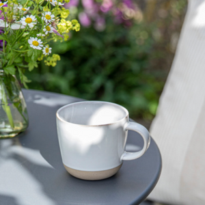 Teacup and vase of flowers on a grey metal tabletop outdoors.